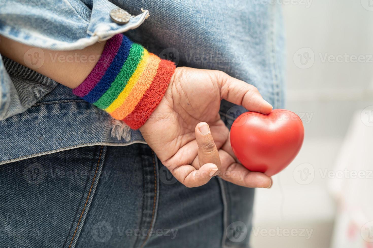 senhora asiática usando pulseiras de bandeira de arco-íris e segurar um coração vermelho, símbolo do mês do orgulho LGBT, comemorar anual em junho social de gays, lésbicas, bissexuais, transgêneros, direitos humanos. foto