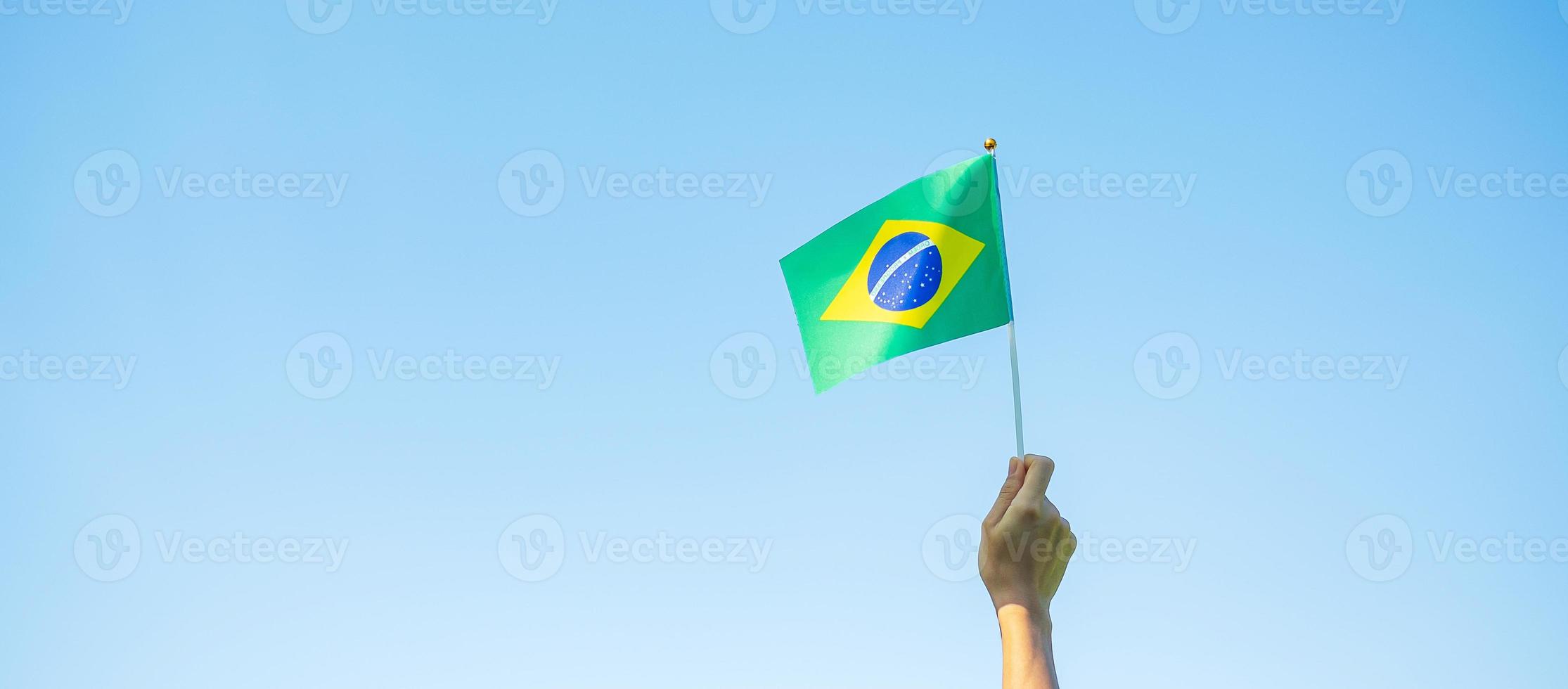 mão segurando a bandeira do brasil sobre fundo de céu azul. dia da independência de setembro e conceitos de celebração feliz foto