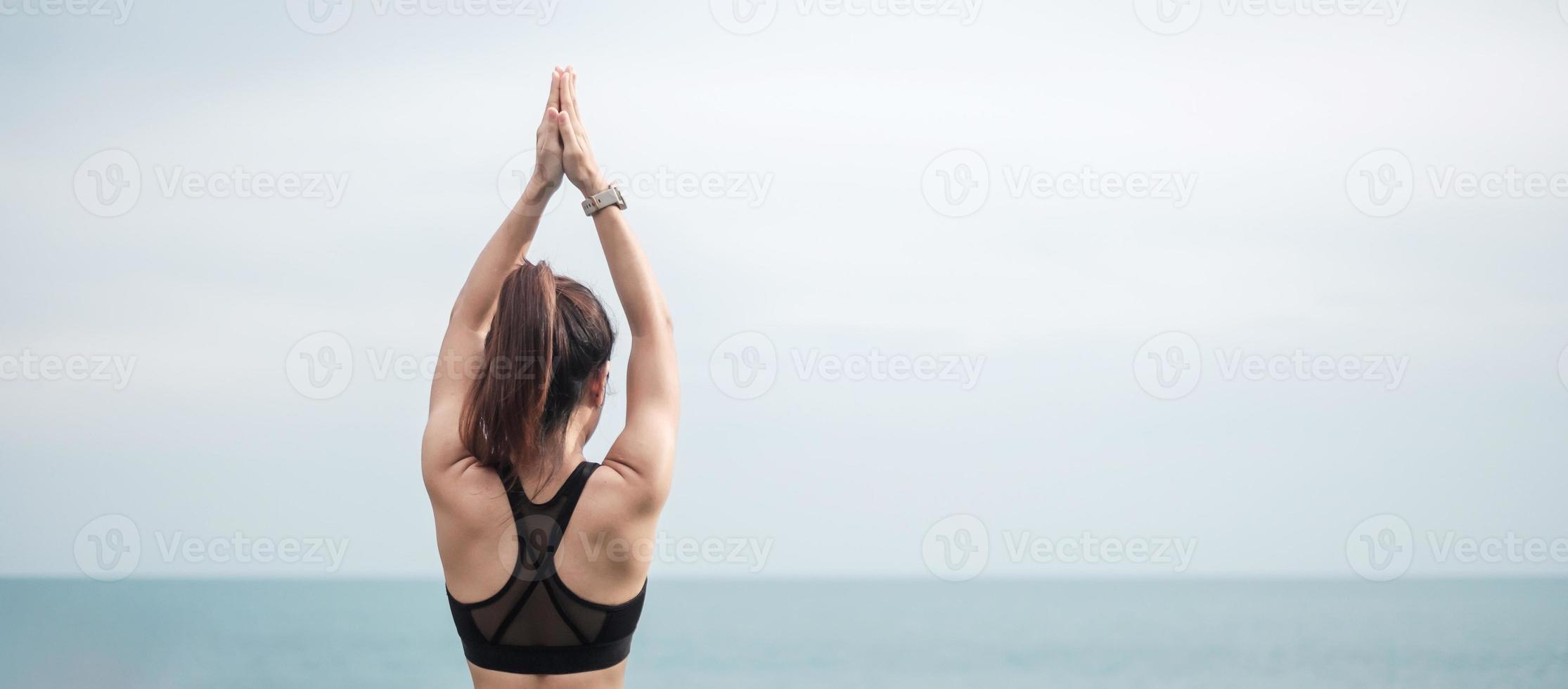 jovem mulher fazendo ioga e alongamento muscular na manhã, meditação menina saudável contra a vista para o mar. conceitos de bem-estar, fitness, vitalidade, exercício e equilíbrio entre vida profissional foto