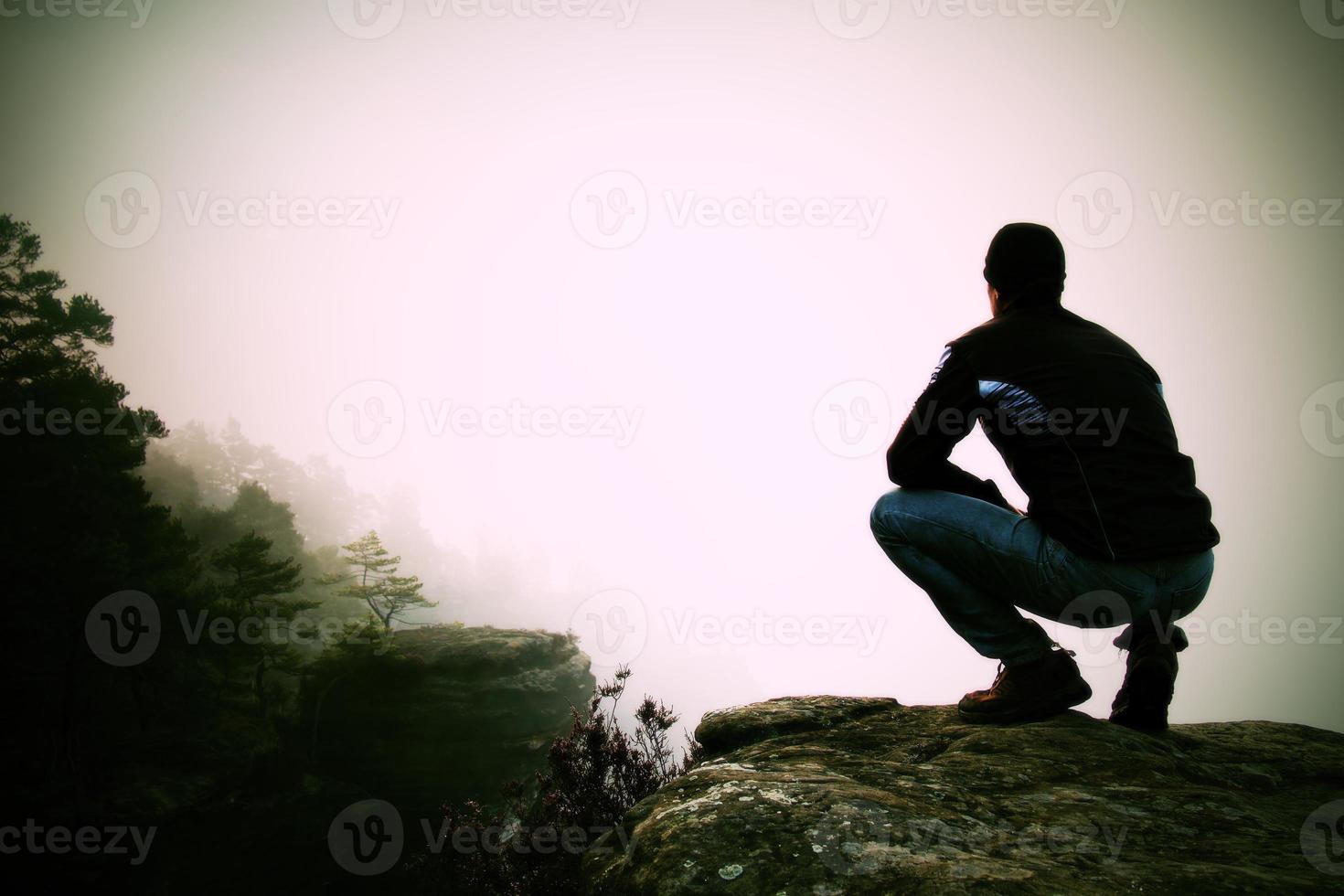 alpinista em posição agachada no pico rochoso e apreciar a paisagem foto