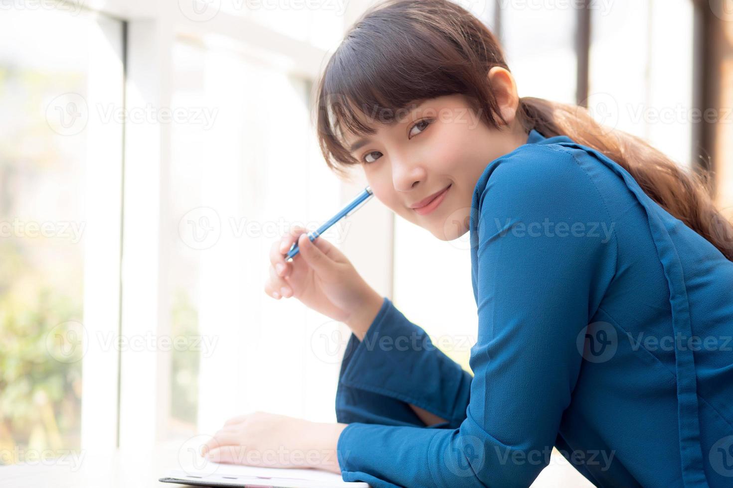 bela jovem escritora asiática sorrindo pensando a ideia e escrevendo no caderno ou diário com feliz, estilo de vida da garota asiática é estudante, planejamento feminino de trabalho, educação e conceito de negócios. foto