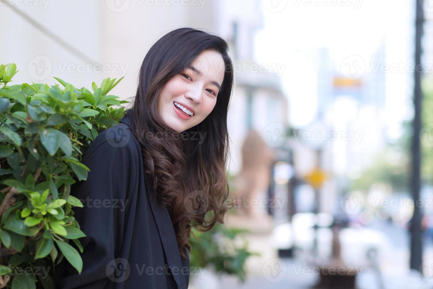 mulher asiática de retrato com cabelo comprido usa casaco preto e fica ao ar livre na cidade. foto