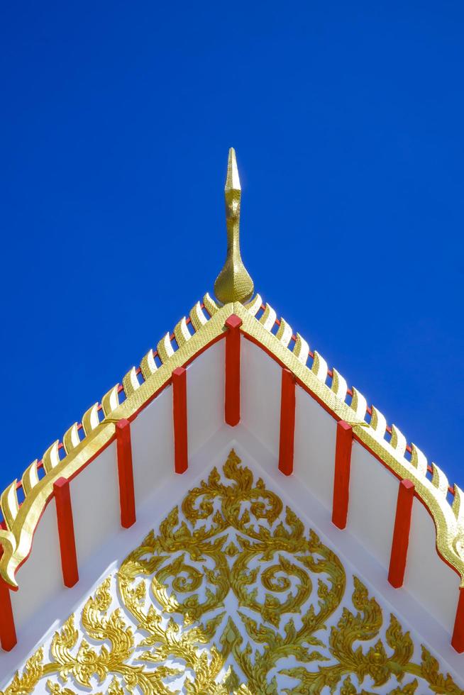 vista de ângulo baixo do ápice do frontão dourado no telhado ornamental do templo tailandês contra o fundo do céu azul claro no quadro vertical foto