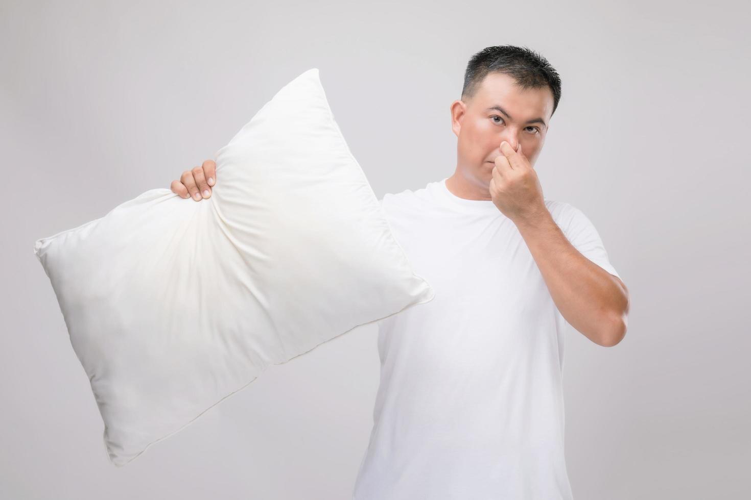 o travesseiro cheira mal. homem asiático de retrato segurando o travesseiro branco e ficando com mau cheiro. estúdio filmado em cinza foto