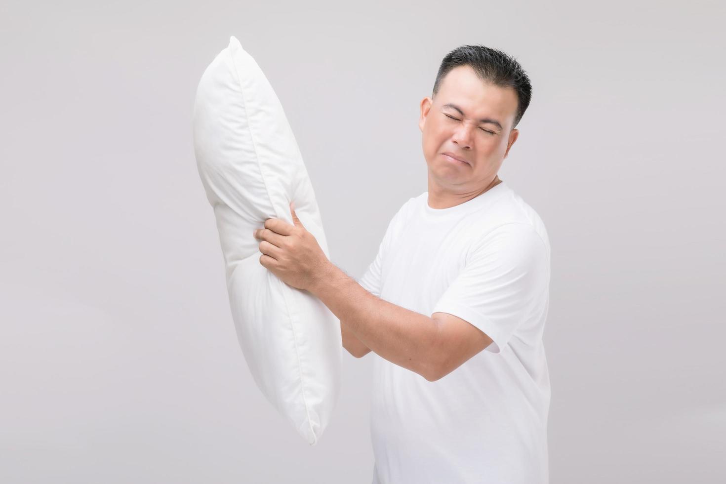 o travesseiro cheira mal. homem asiático de retrato segurando o travesseiro branco e ficando com mau cheiro. estúdio filmado em cinza foto