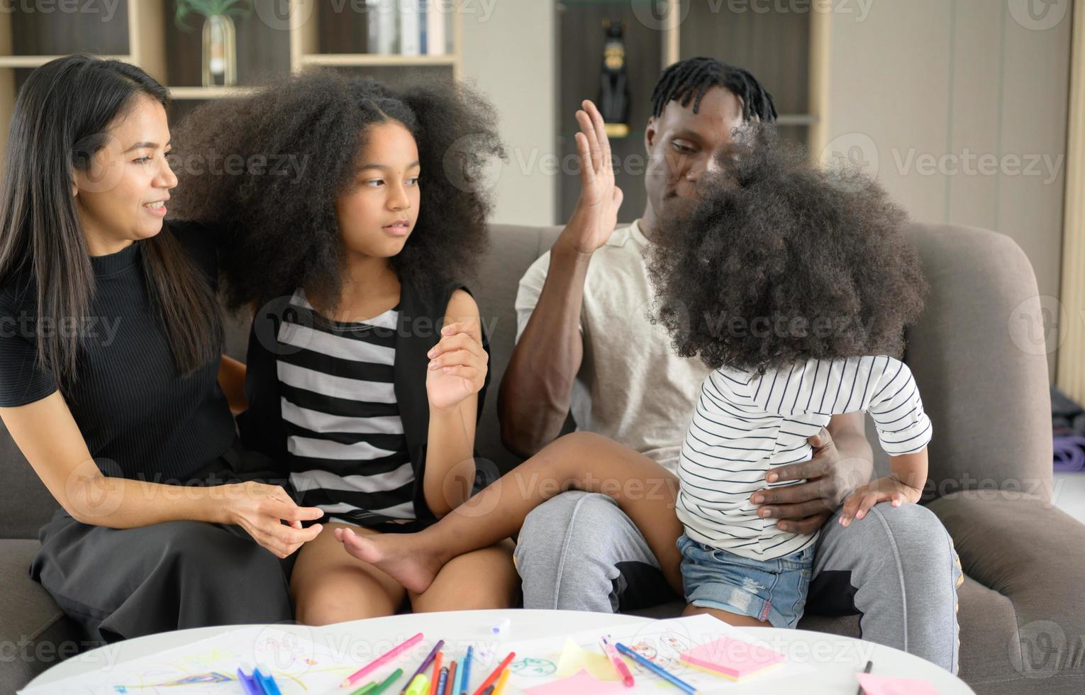 família afro-americana relaxando, conversando, pintando e se divertindo nas férias na sala de estar da casa foto