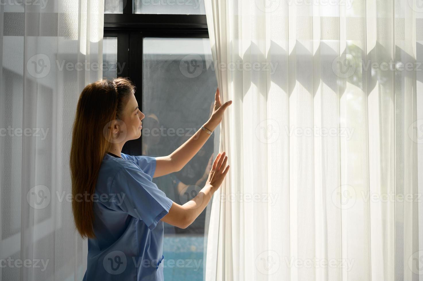 enfermeira asiática abre as cortinas da sala de estar para permitir que a luz chegue ao quarto antes de trazer o paciente para se sentar nesta sala de estar. foto