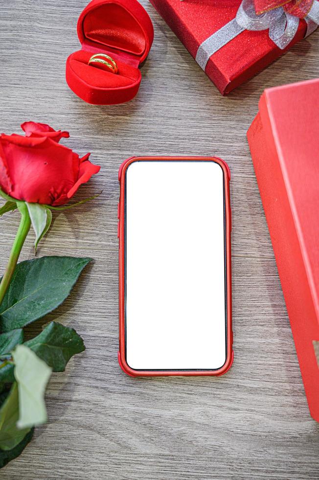 tela branca em branco do telefone com caixas de presente, rosa e anel em fundo de madeira. foto