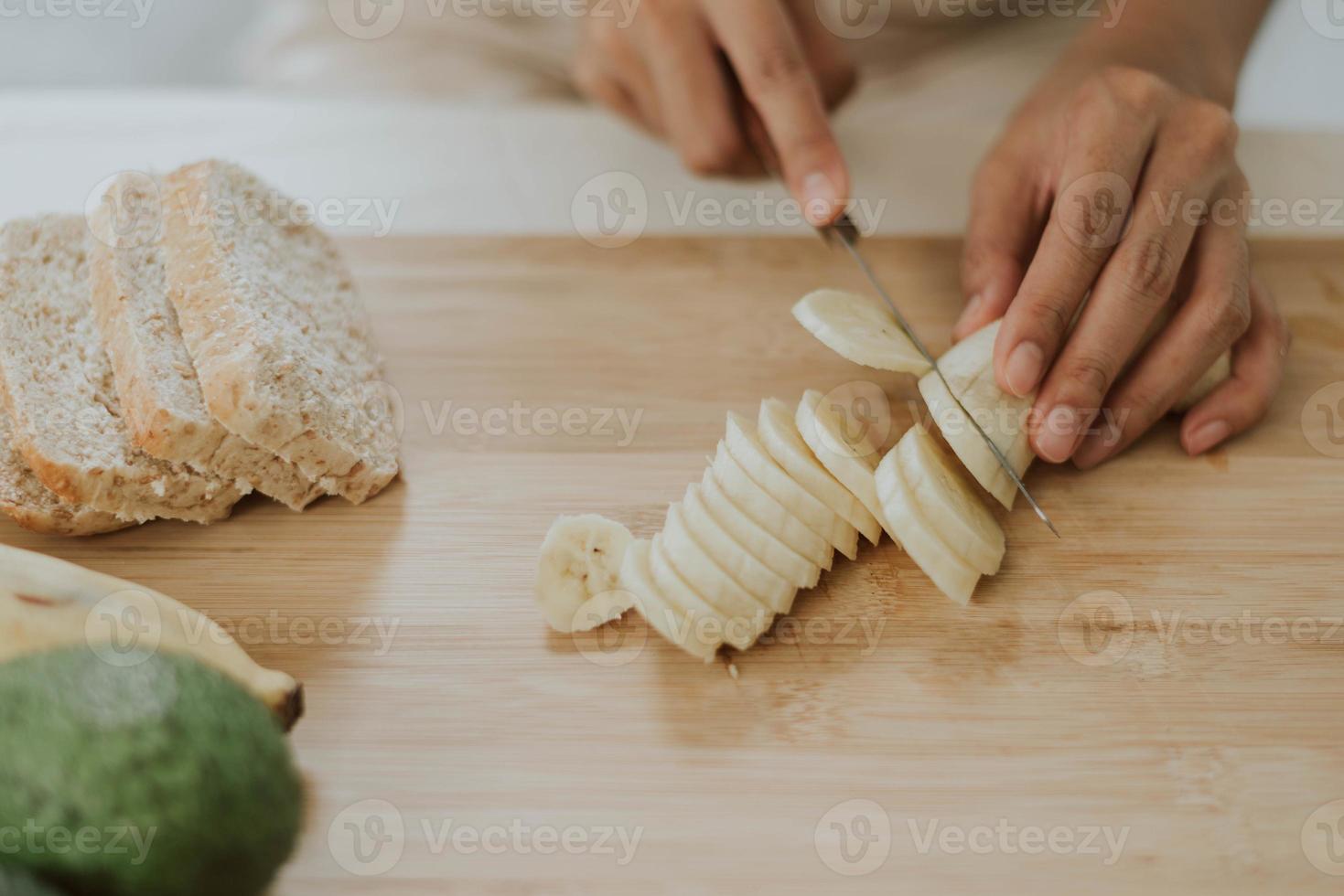 close-up de mãos cortando babana. jovem mulher cozinhando comida saudável em casa. conceito de saúde e bem-estar. foto