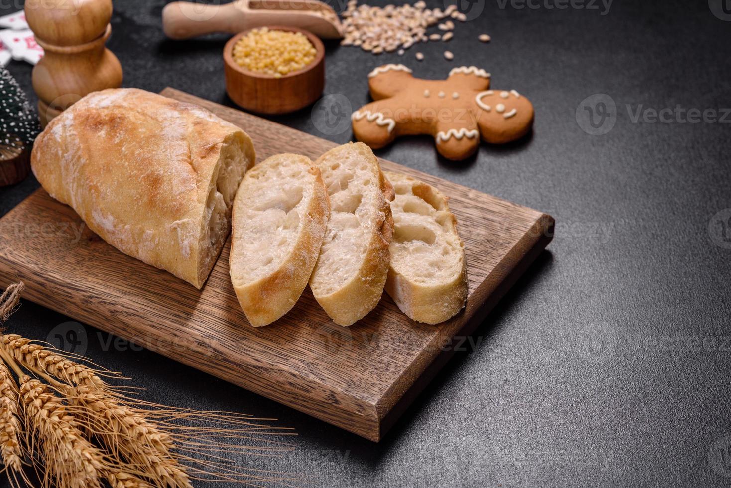 pão baguete francês fatiado em uma tábua de madeira contra um fundo escuro de concreto foto