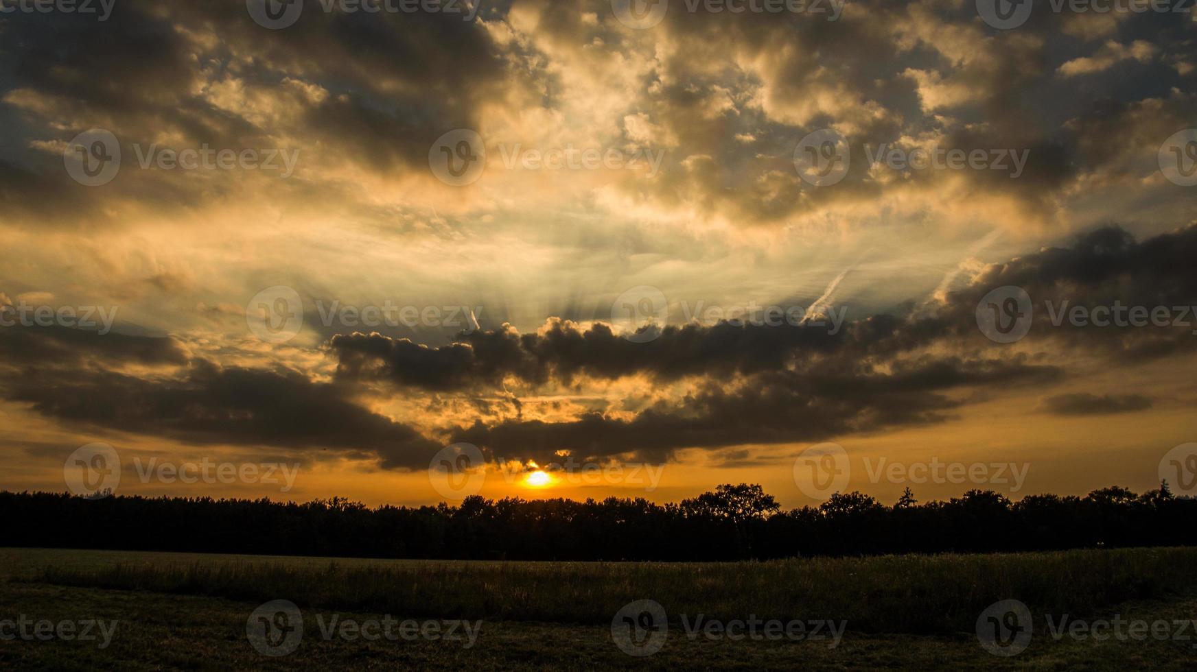 dramático pôr do sol na borda de uma floresta em frente a um campo foto