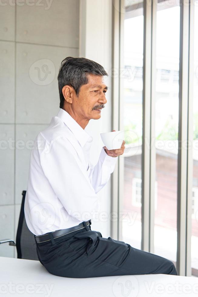 velho de negócios asiáticos com camisa branca trabalhando e tomando café na sala de reuniões no escritório foto