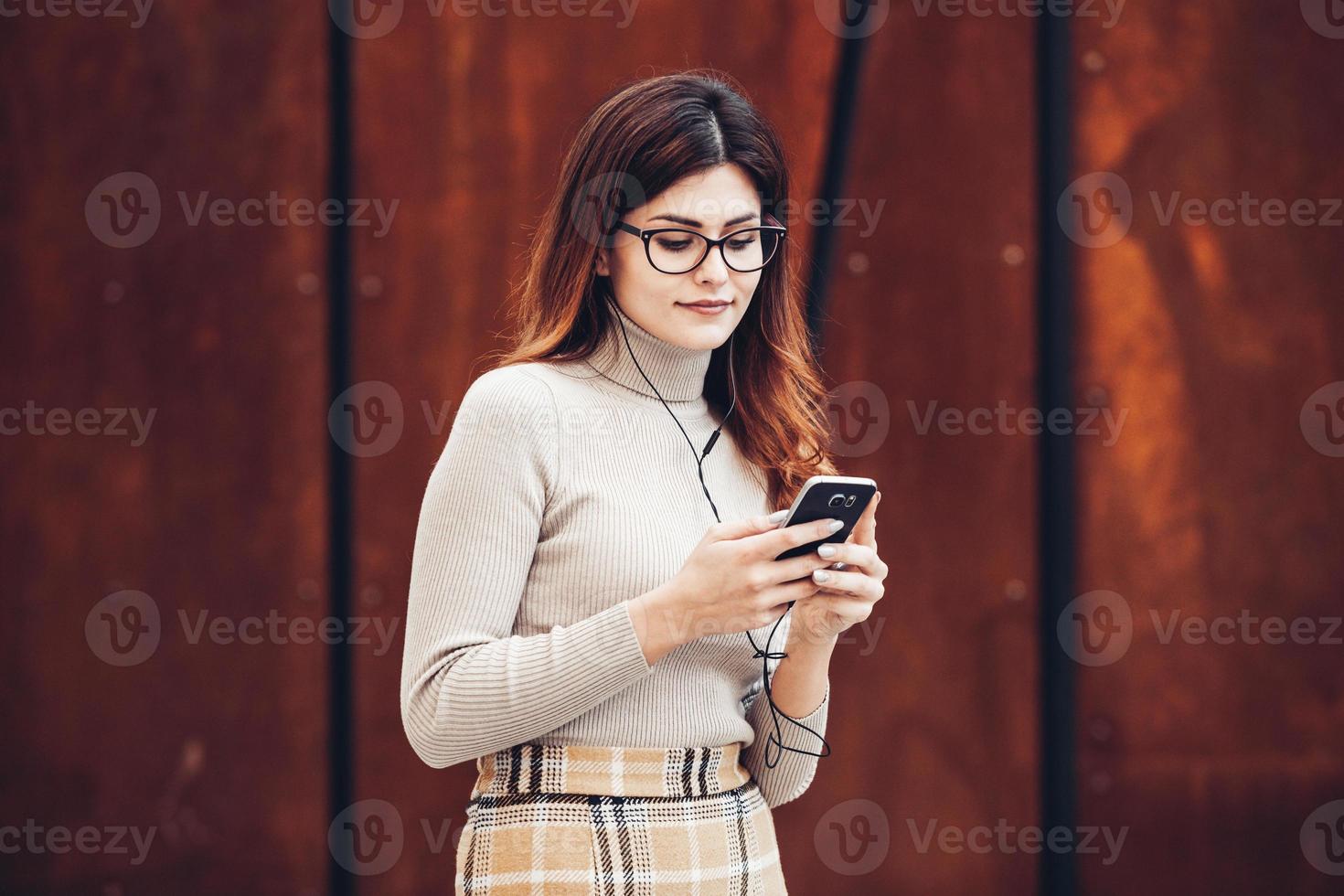 imagem de mulher bonita e elegante segurando o celular. jovem garota europeia parado na rua e usando o celular. mulher ouvindo música com o telefone e se divertindo. conceito de internet móvel. foto