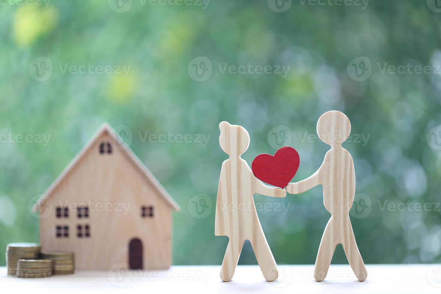 casal de amor segurando forma de coração e pilha de dinheiro de moedas com casa modelo em fundo verde natural, economizando para amante ou família e economize dinheiro para se preparar no futuro conceito foto