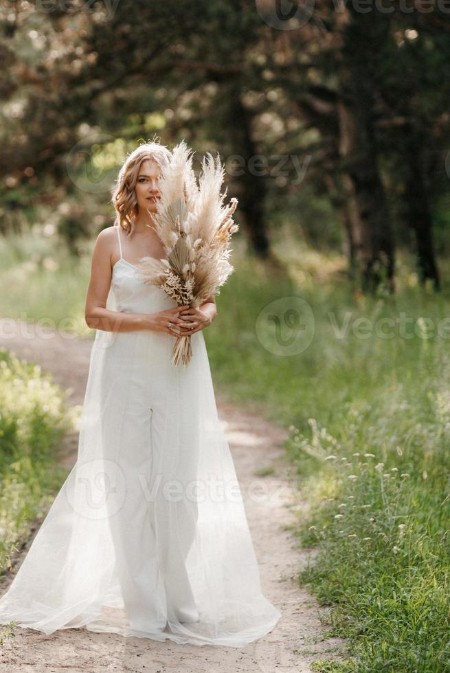 menina noiva feliz em um vestido branco claro com um buquê de flores secas foto