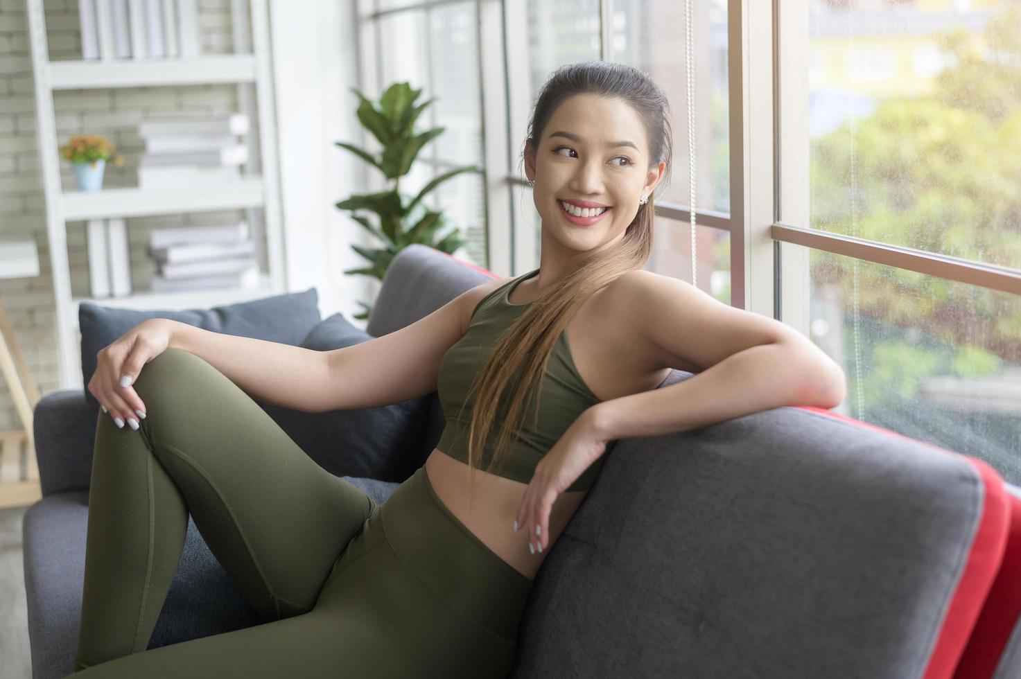 caber linda mulher asain em roupas esportivas sentada e relaxando no sofá após treino, saúde e conceito de exercício foto