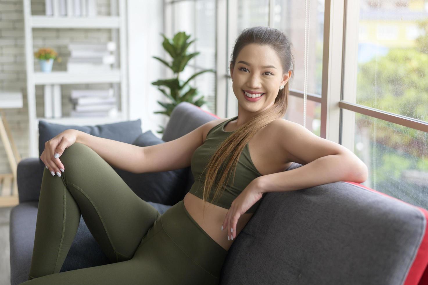 caber linda mulher asain em roupas esportivas sentada e relaxando no sofá após treino, saúde e conceito de exercício foto