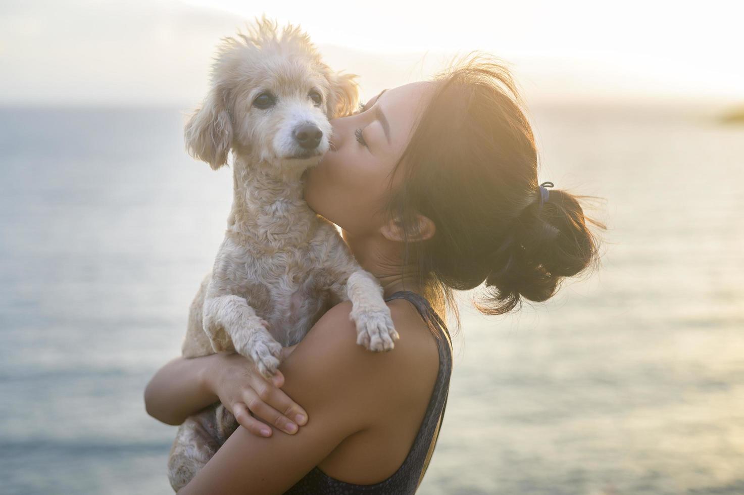 jovem mulher bonita com seu cachorro curtindo e relaxando à beira-mar durante o pôr do sol, verão, férias, feriados, conceito de estilos de vida. foto