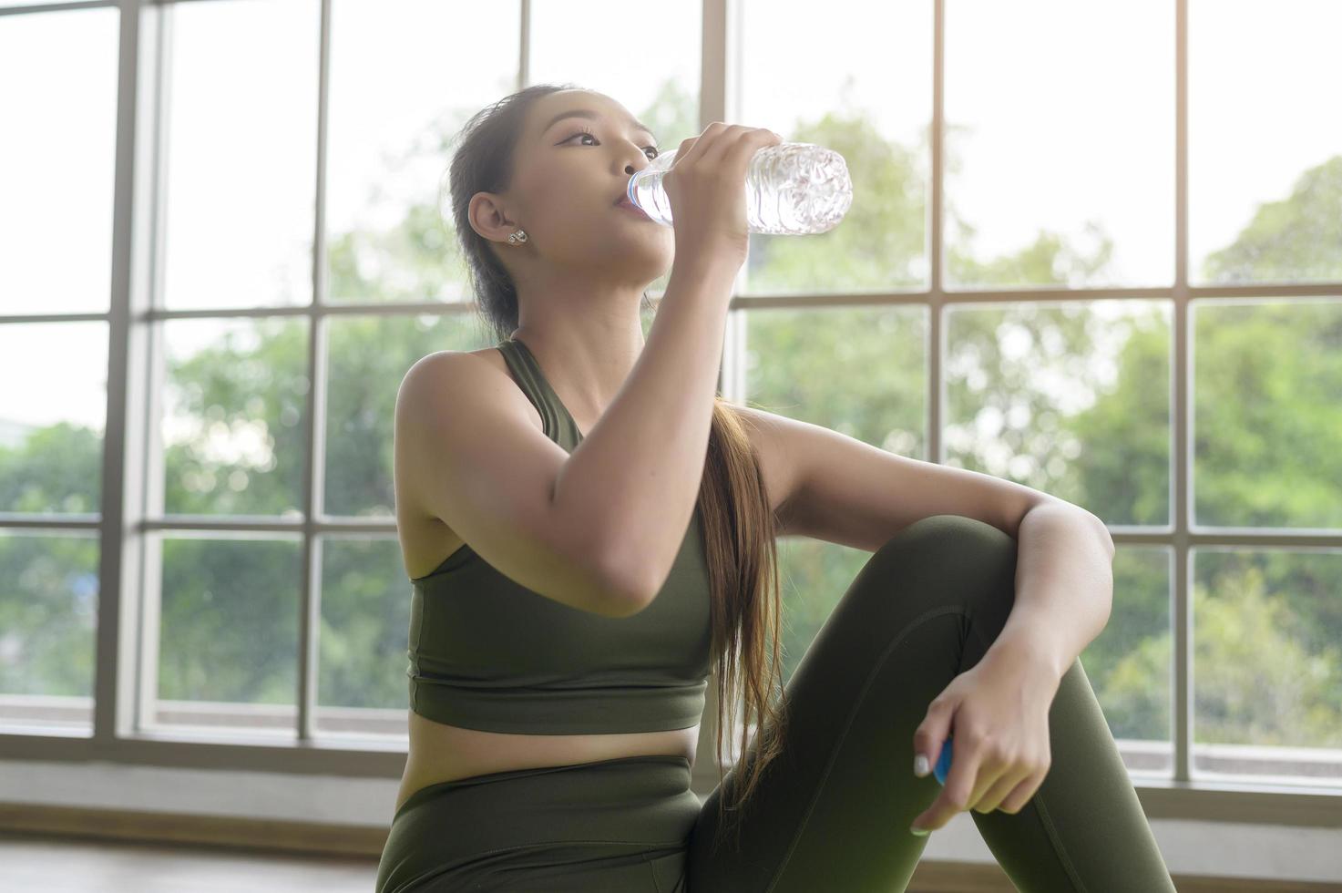 mulher jovem fitness em sportswear água potável após o exercício em casa, saudável e estilos de vida. foto