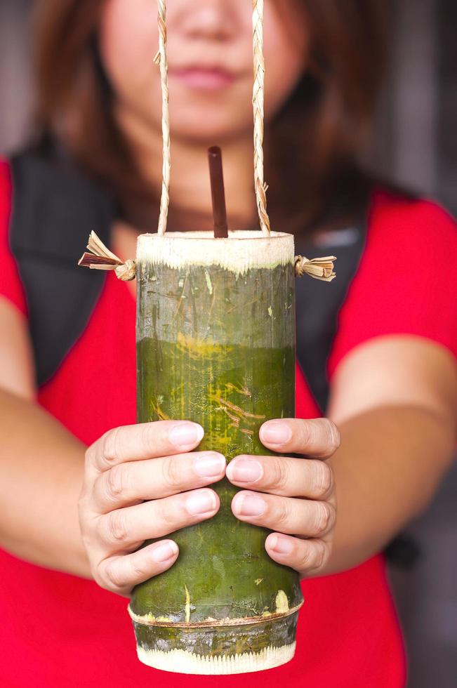 uma senhora está dando bebida em um recipiente de copo de bambu, estilo tradicional tailandês. foto está focada em alguma parte de um copo.