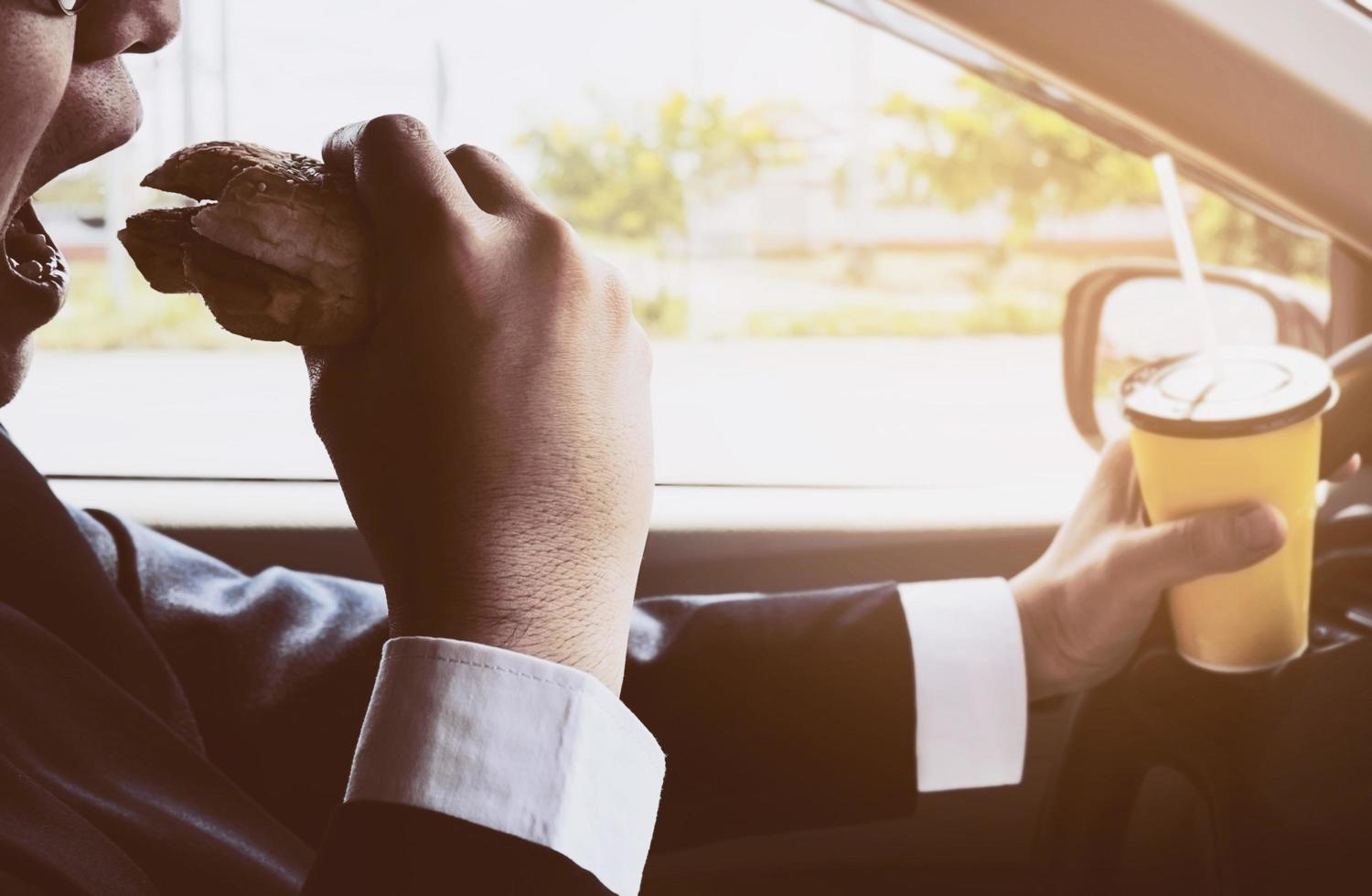 homem dirigindo carro segurando uma xícara de café frio e comendo hambúrguer foto