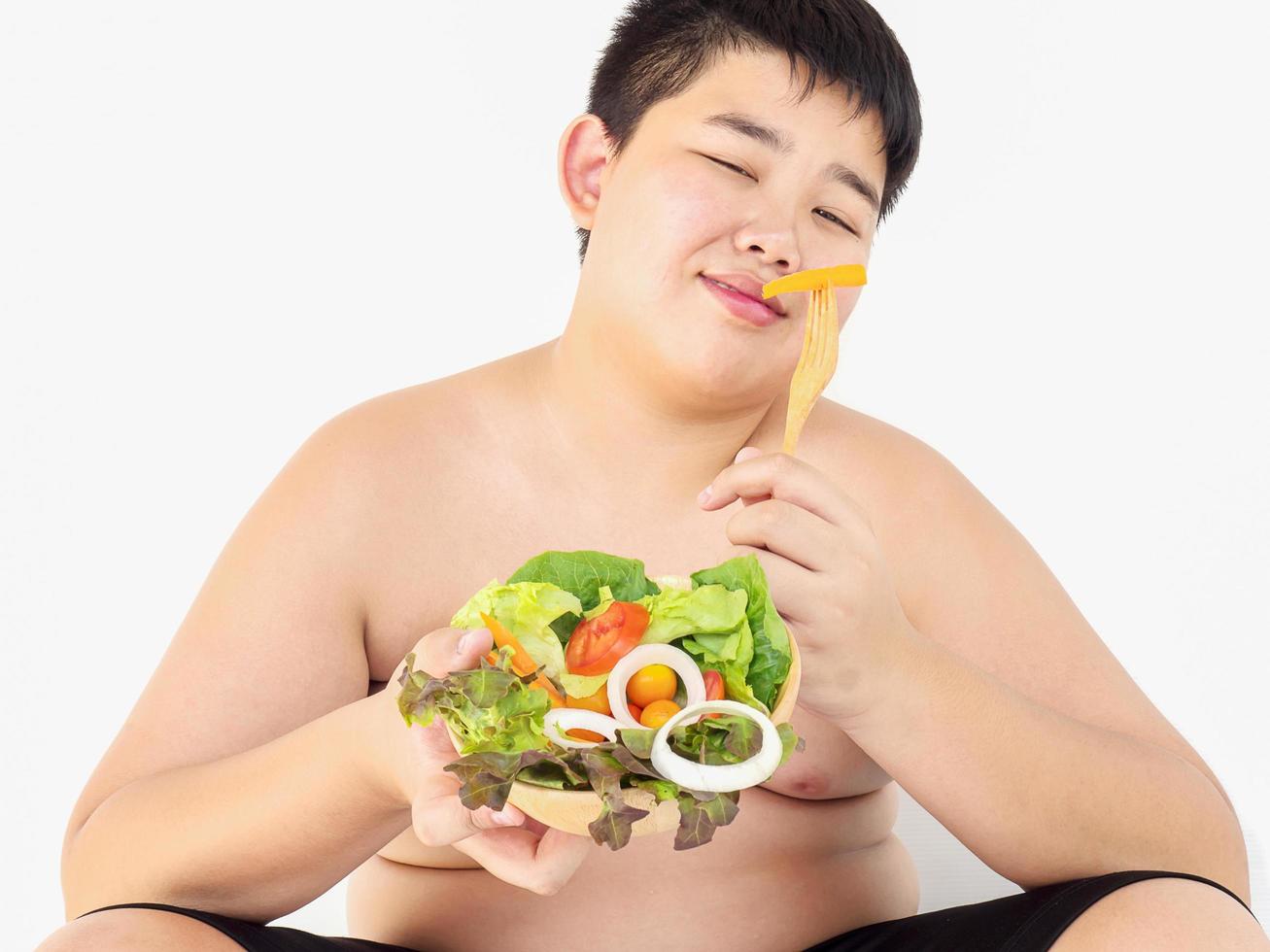 um menino gordo está comendo alegremente salada de legumes foto