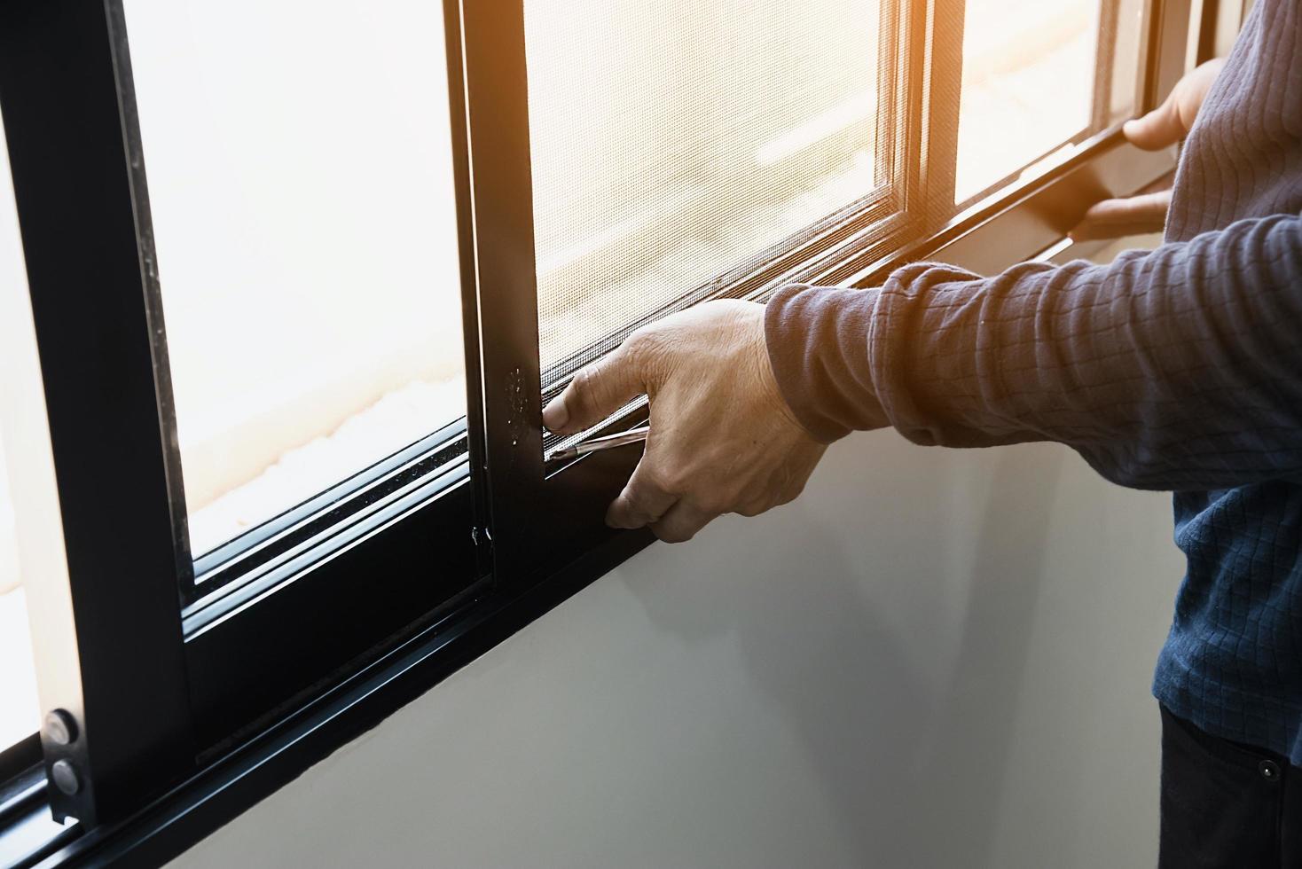 homem fazendo armação de alumínio com óculos e tela de arame trabalho de instalação de porta e janela no canteiro de obras foto