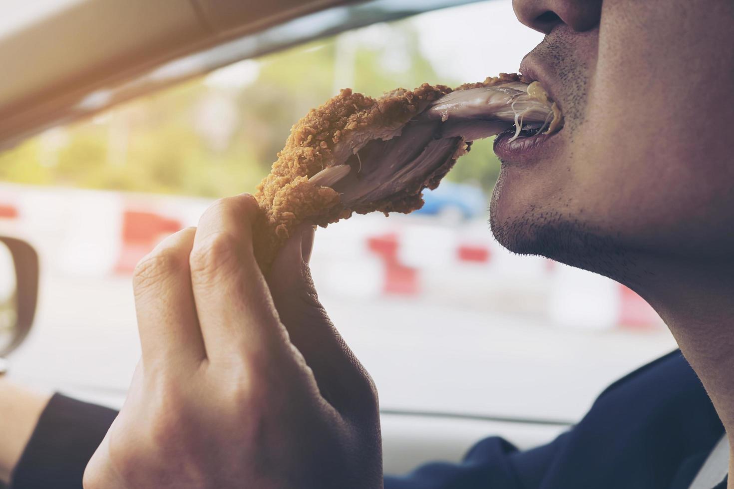 homem de negócios dirigindo carro enquanto come frango frito perigosamente foto