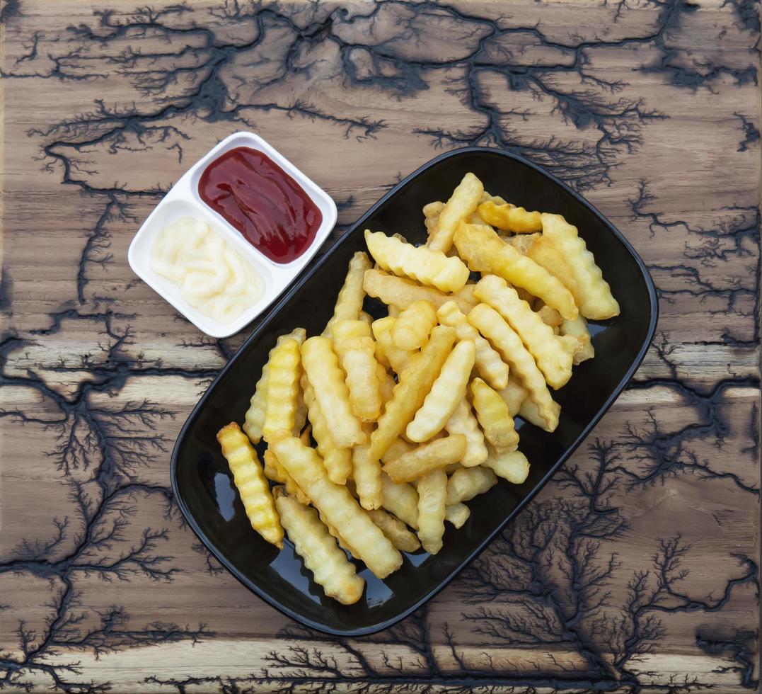 vista lateral de batatas fritas com molhos na placa de madeira foto