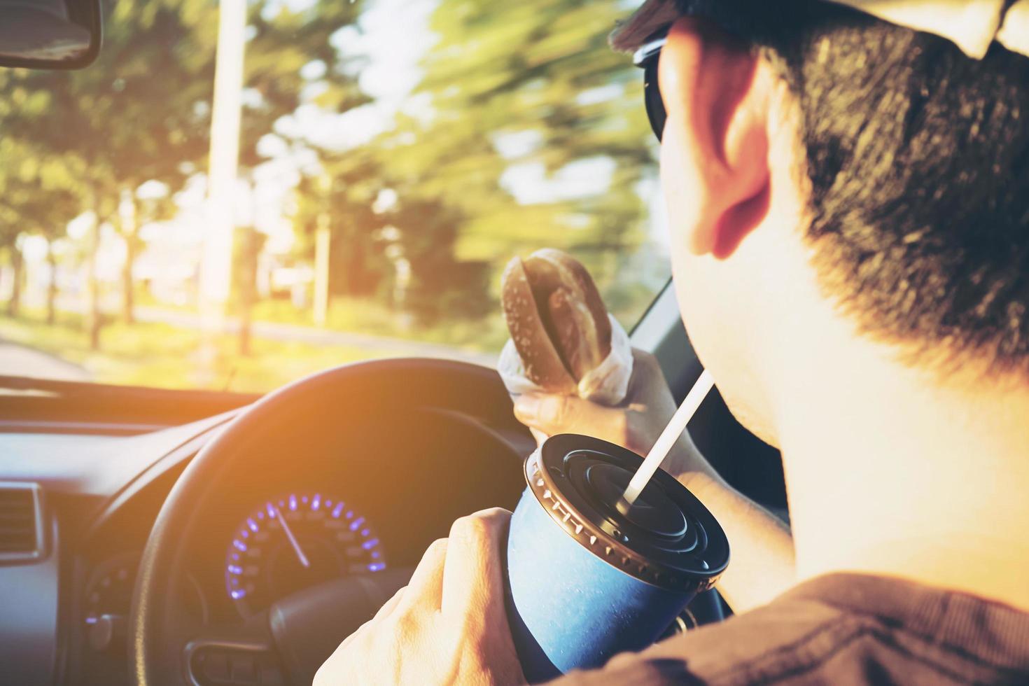 homem está comendo perigosamente cachorro-quente e bebida gelada enquanto dirige um carro foto