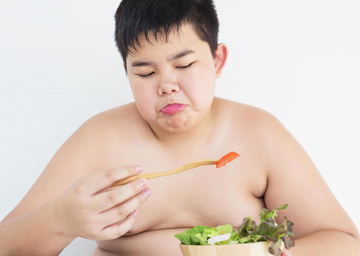 um menino gordo odeia comer salada de legumes foto