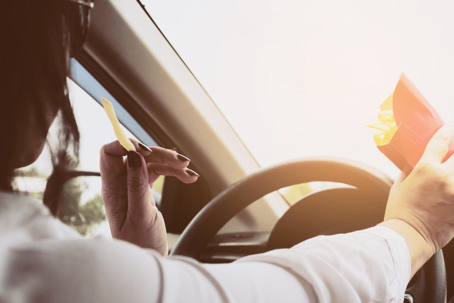 senhora comendo batatas fritas branco dirigindo carro perigosamente foto