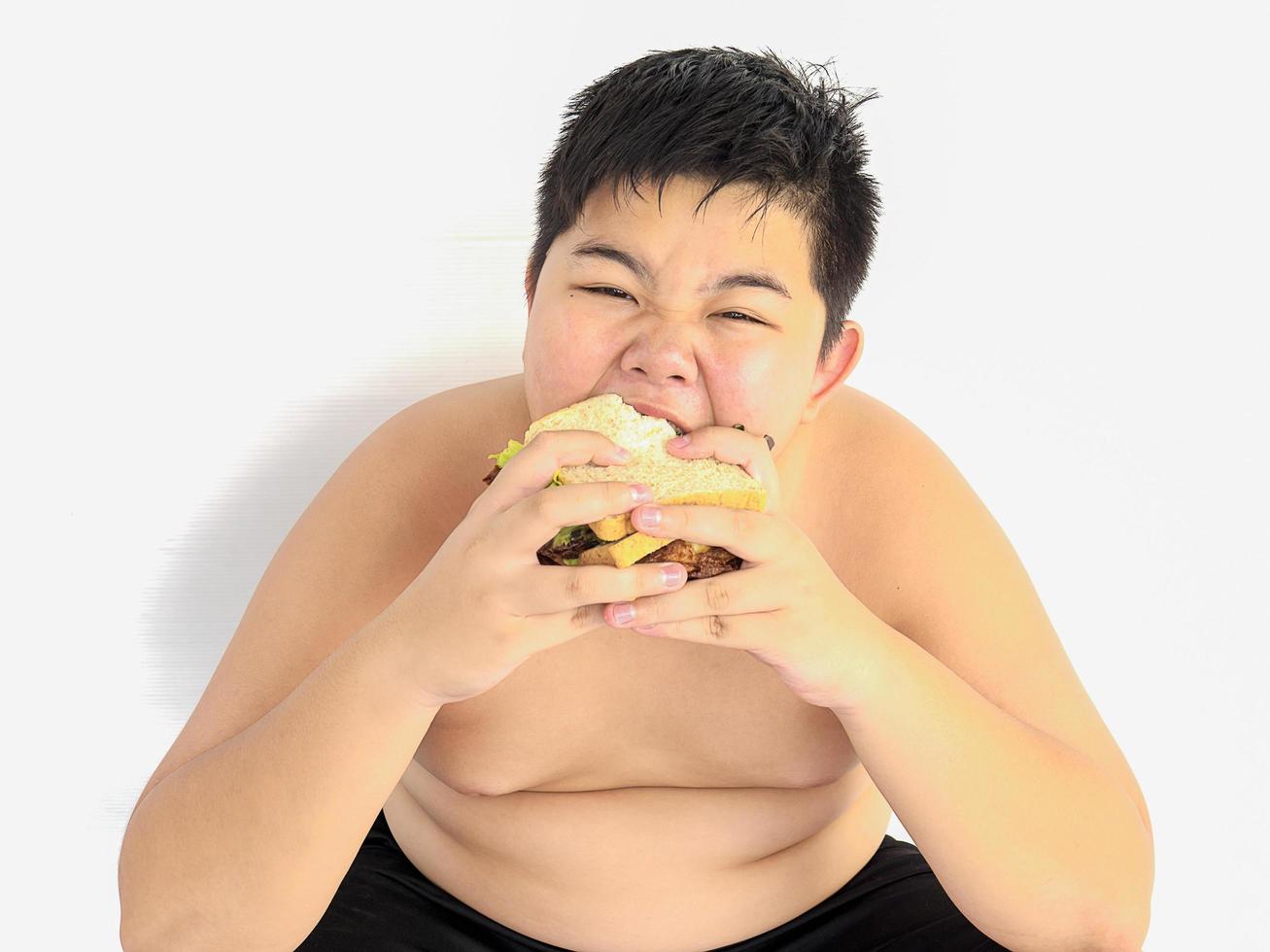 um menino gordo está comendo sanduíche alegremente. foto