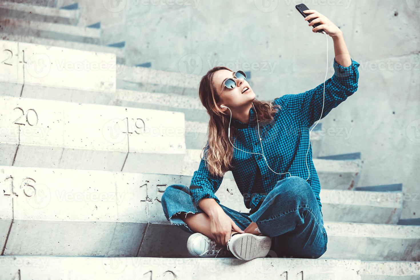 foto de uma jovem estudante bonita sorridente alegre usando óculos escuros ao ar livre usando telefone celular conversando ouvindo música com fones de ouvido.