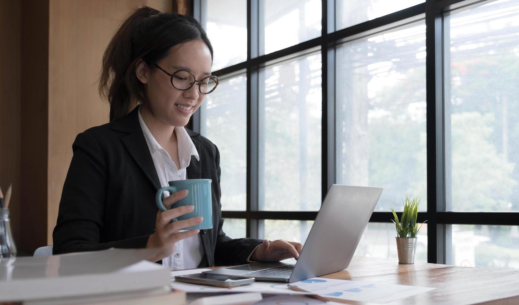 jovem empresária asiática tem o prazer de ver o trabalho em seu tablet e café favorito no escritório. foto