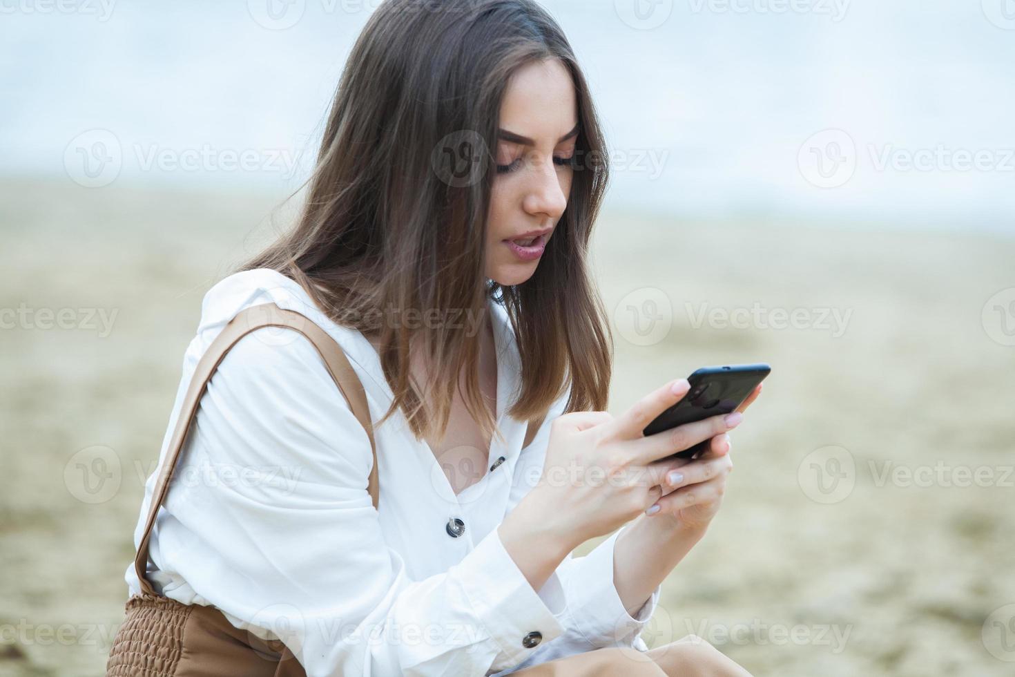 garota ao ar livre mensagens de texto em seu celular. menina com telefone. retrato de uma mensagem de sms de texto de mulher feliz em seu telefone. foto