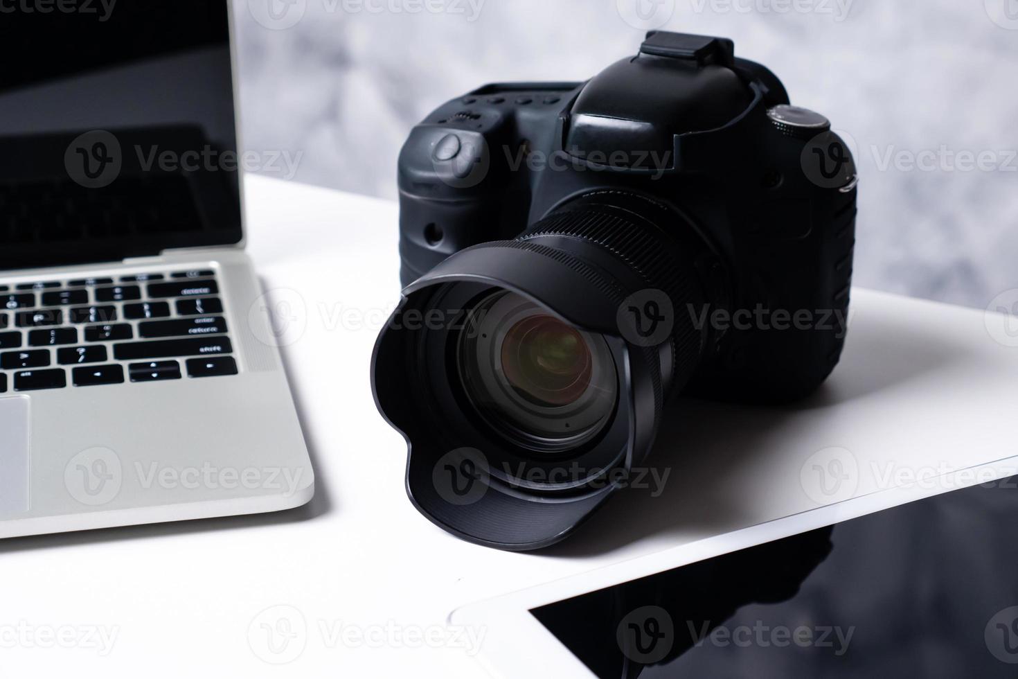 uma câmera digital preta, um tablet e um laptop em uma mesa. foto