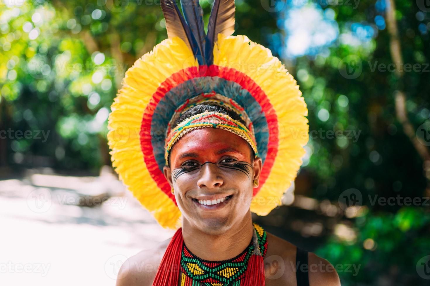 índio da tribo pataxo com cocar de penas olhando para a câmera. homem indígena do brasil, com pinturas faciais tradicionais foto