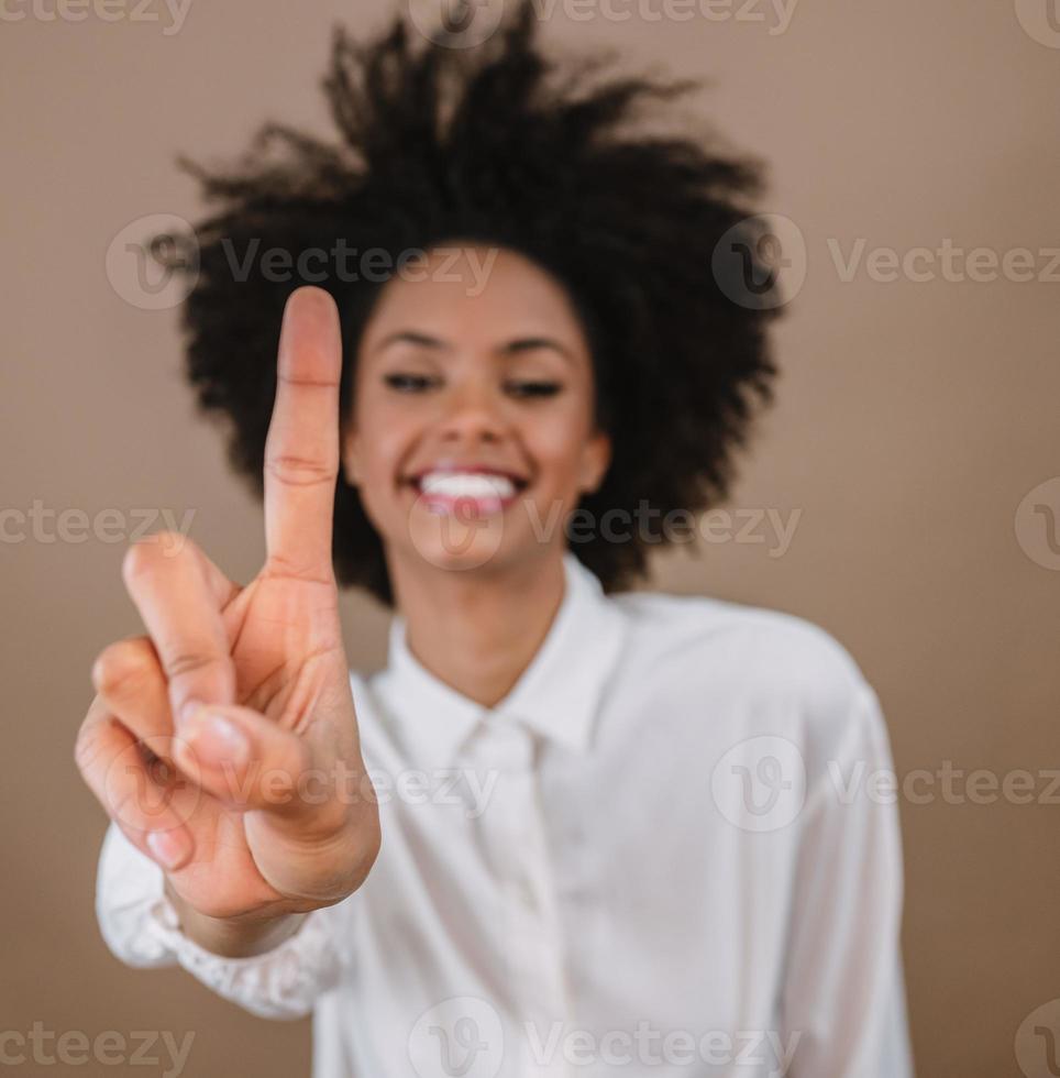 mulher latina sorridente fazendo um, primeiro gesto de sinal de contagem regressiva com os dedos da mão no fundo pastel. foto