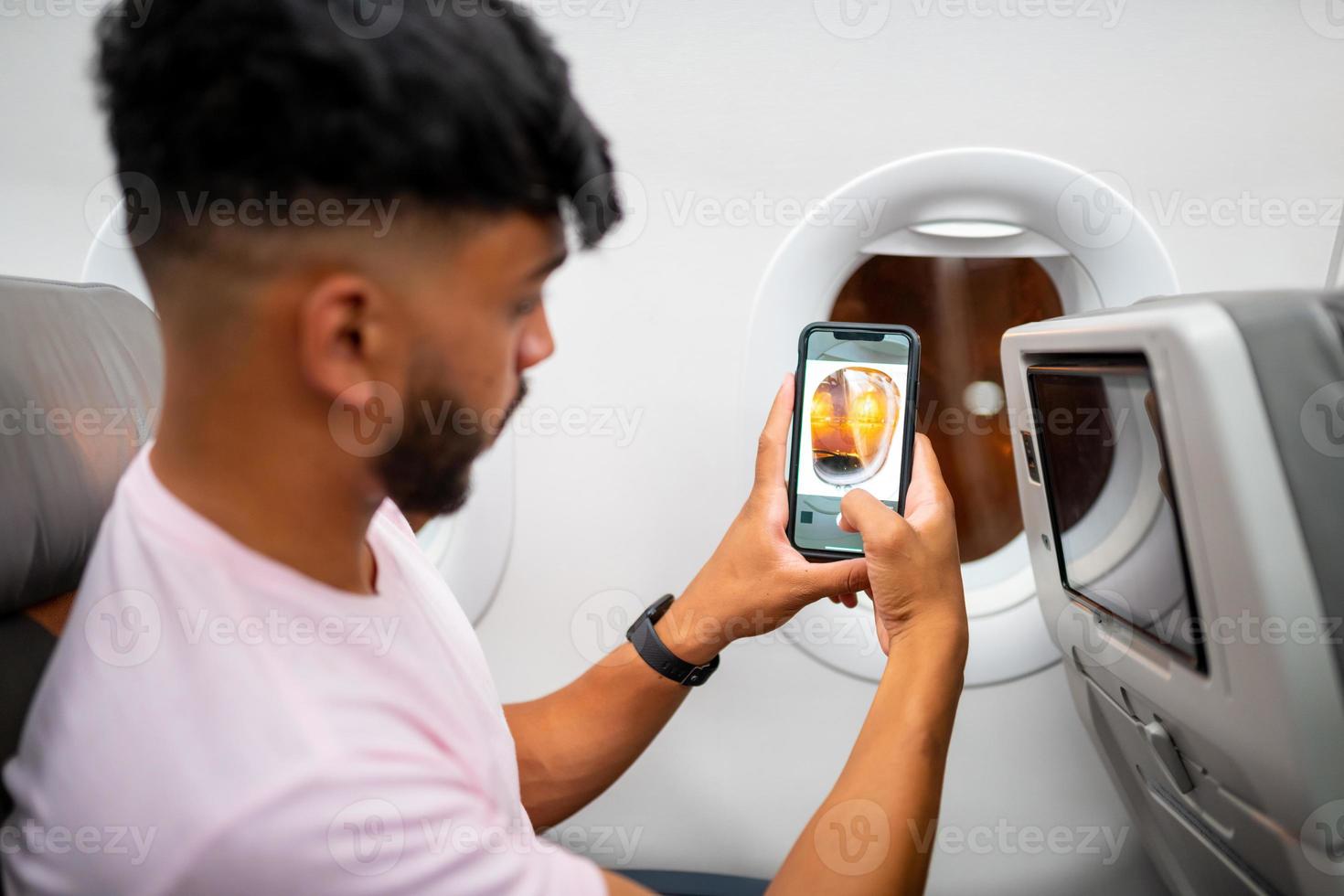 jovem latino-americano fazendo uma chamada de vídeo no celular, sentado no avião perto da janela. foto
