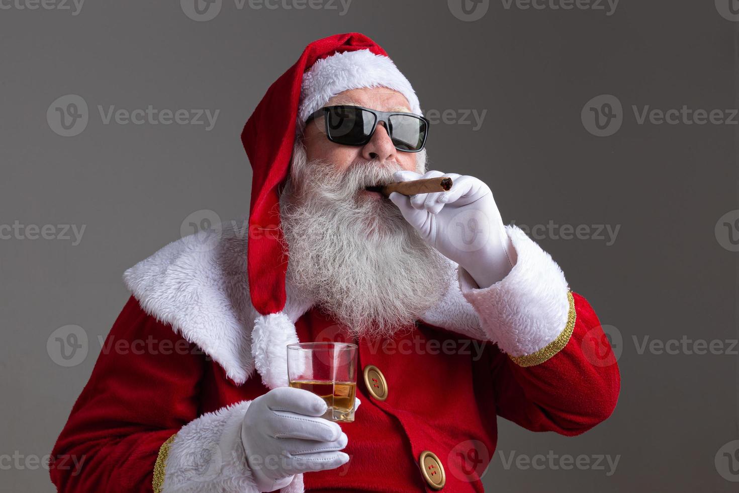 papai noel usando óculos escuros fumando um charuto e bebendo batedor em fundo escuro foto