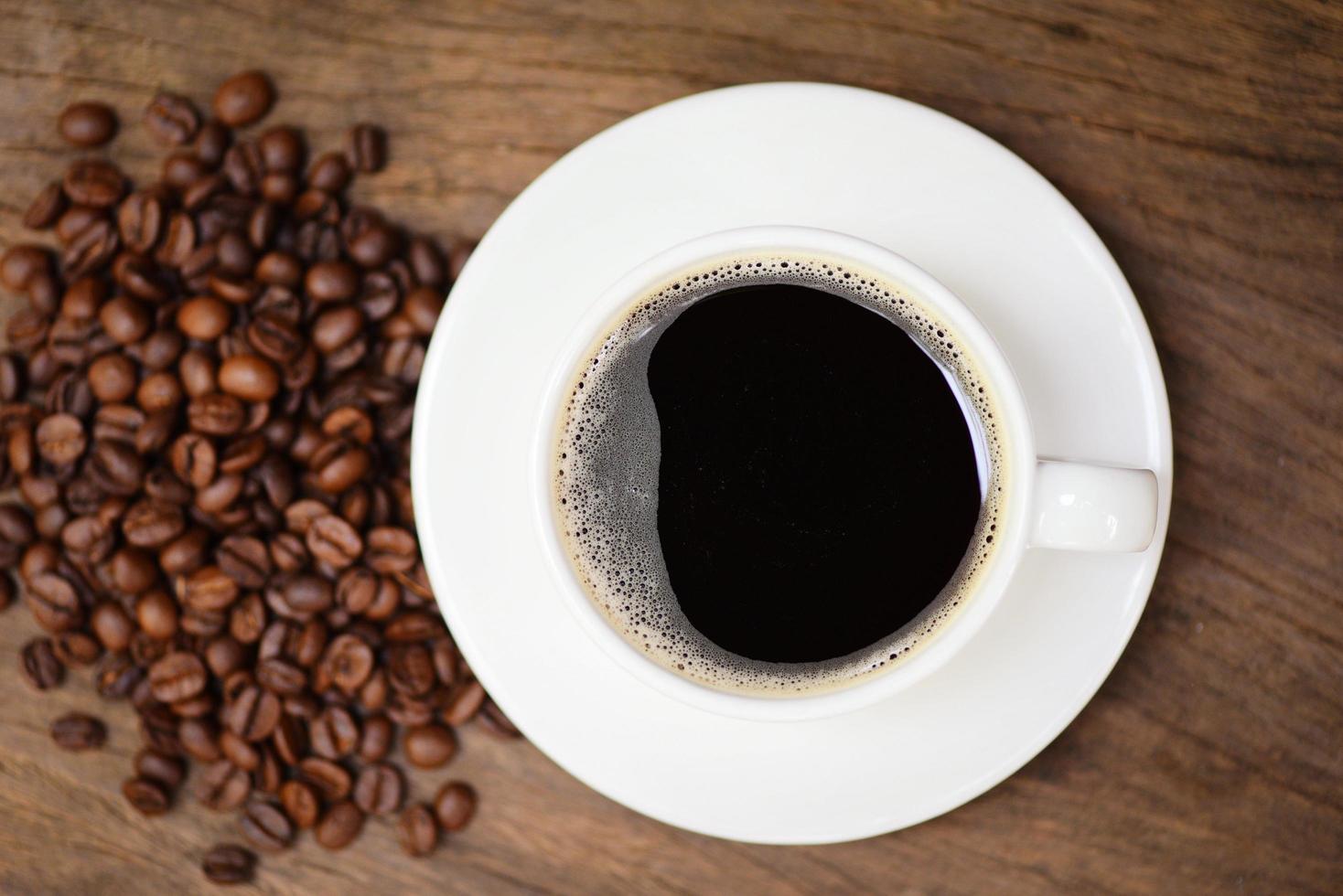xícara de café e grãos de café na mesa café preto em caneca branca sobre fundo de madeira foto
