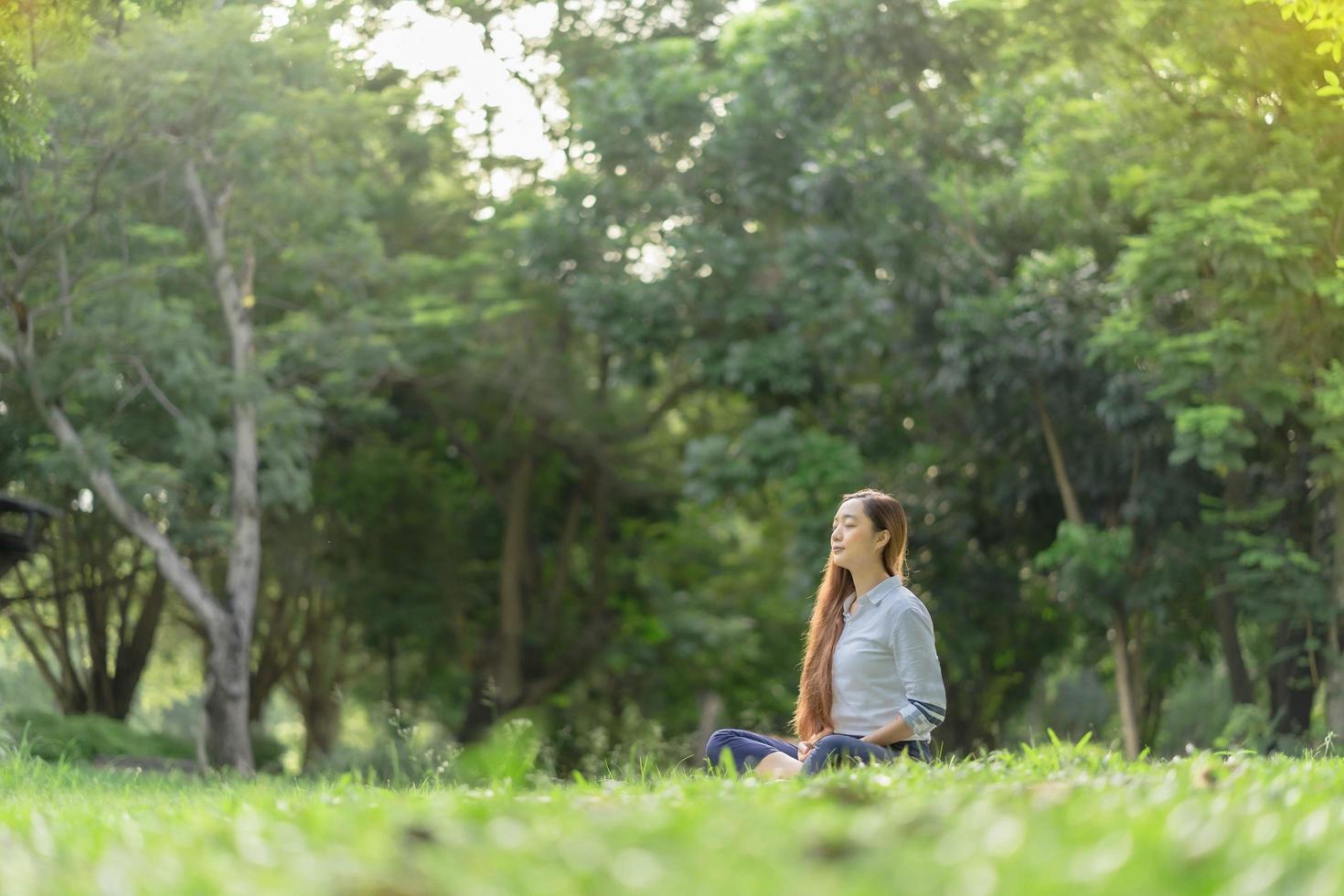 mulher feliz fazendo meditação e relaxando no parque. meditação na natureza. conceito de estilo de vida saudável e relaxamento. mulher bonita praticando meditação na grama foto