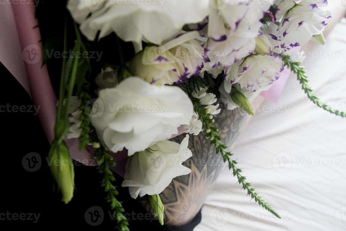 flores brancas, buquê em um lençol branco, tatuagem de perna preta foto