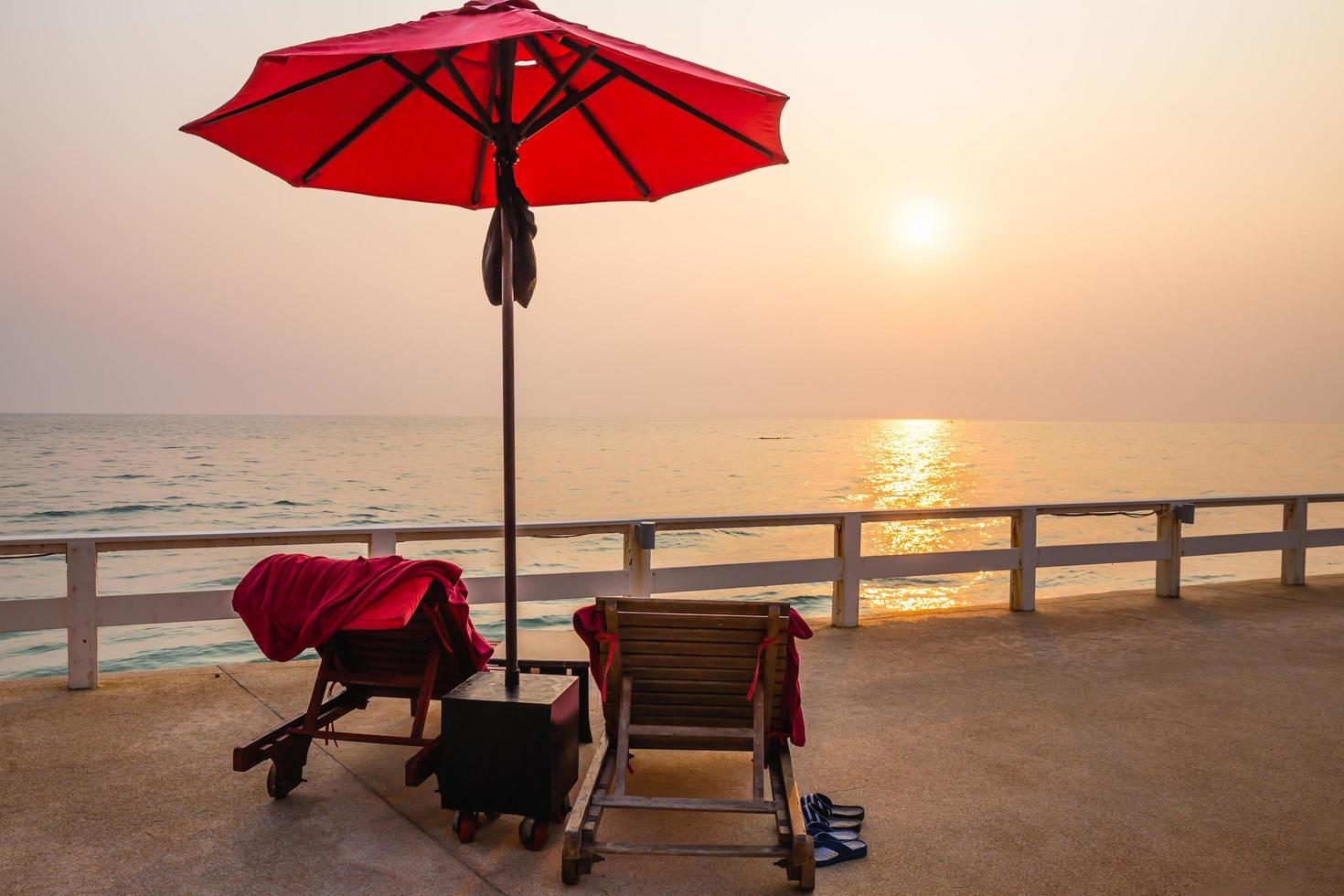 guarda-chuva vermelho e cadeiras de piscina na hora do nascer do sol ao redor da piscina ao ar livre. foto