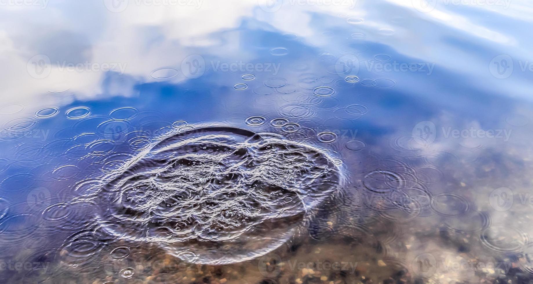 bela água em um lago com salpicos de água e ondulações na superfície com nuvens e reflexos do céu azul foto