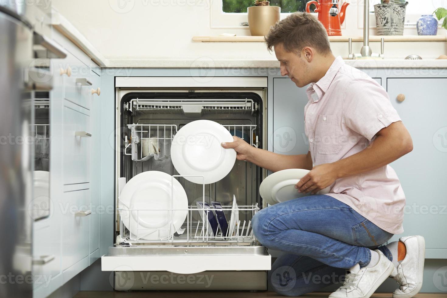 homem carregando máquina de lavar louça na cozinha foto