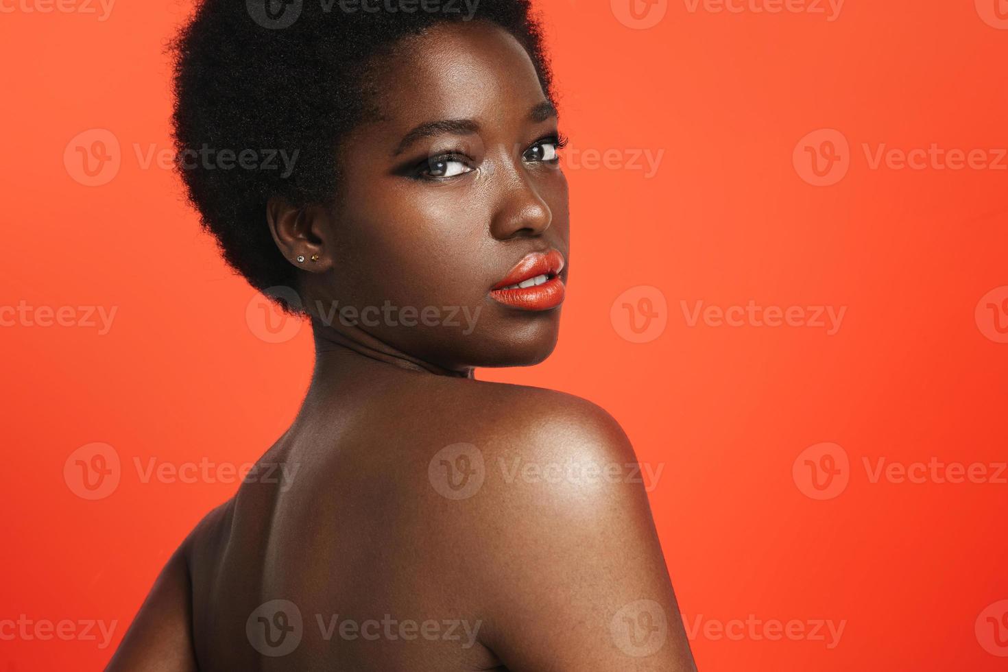 mulher negra usando lábios brilhantes em um fundo laranja brilhante foto