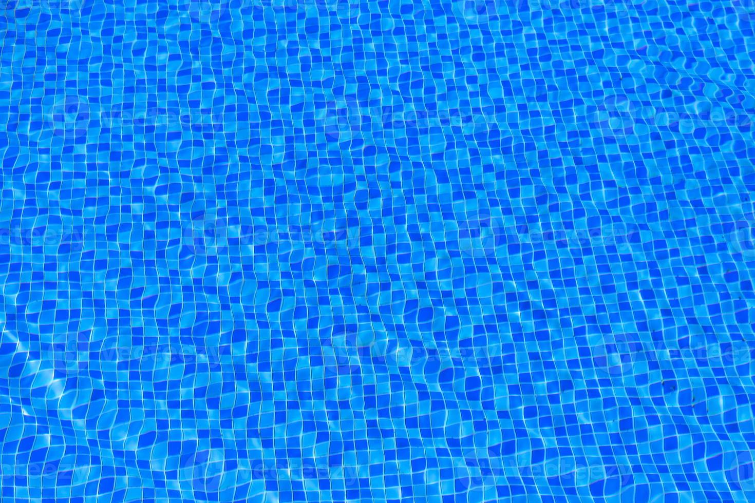 ondulações de água no fundo da piscina de azulejos azuis. água da piscina azul turquesa. ondas iluminadas pelo sol. telhas visíveis abaixo. vista do topo foto