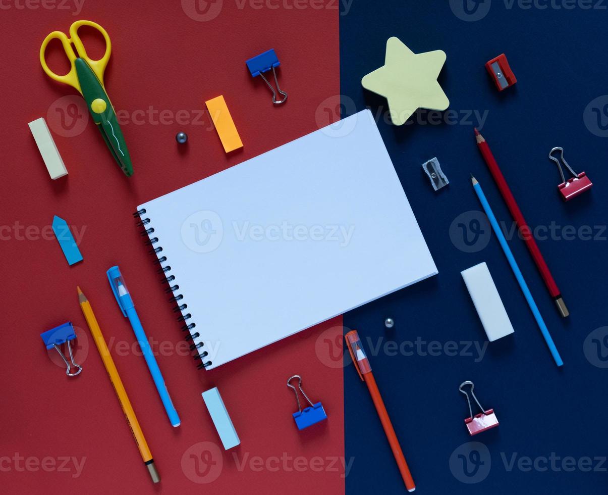 de volta ao conceito de escola. material escolar e de escritório na mesa do escritório. fundo azul e vermelho. vista plana leiga de cima foto